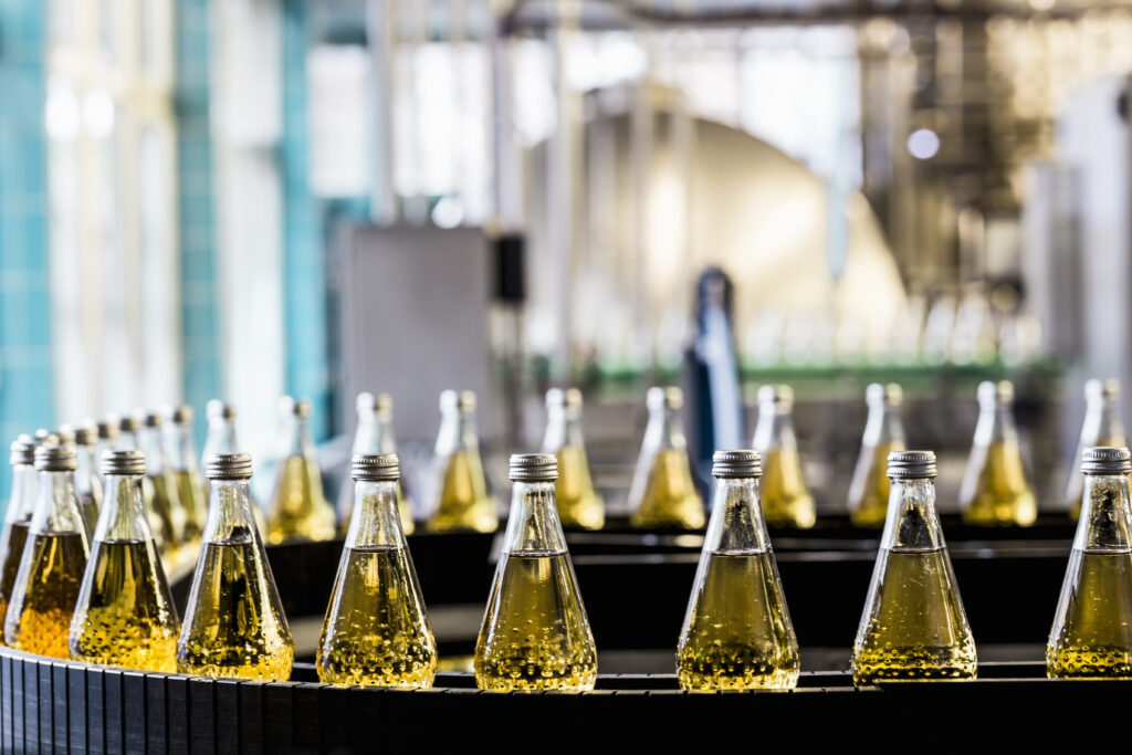 rows of goldenhued liquid bottles with a person blurred in the background at a factory.
